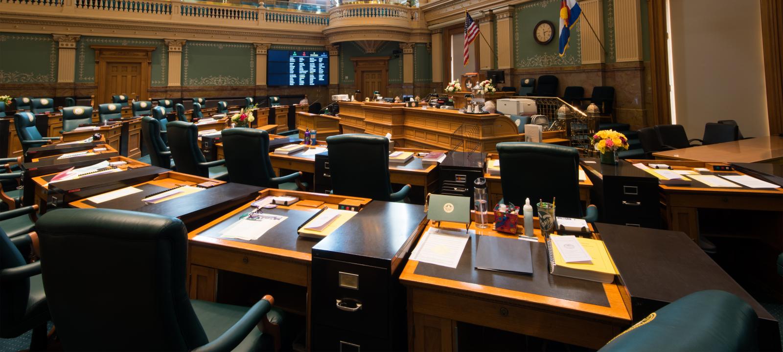 View from the House chamber floor showing desk of representatives organized in a half-circle around the main podium